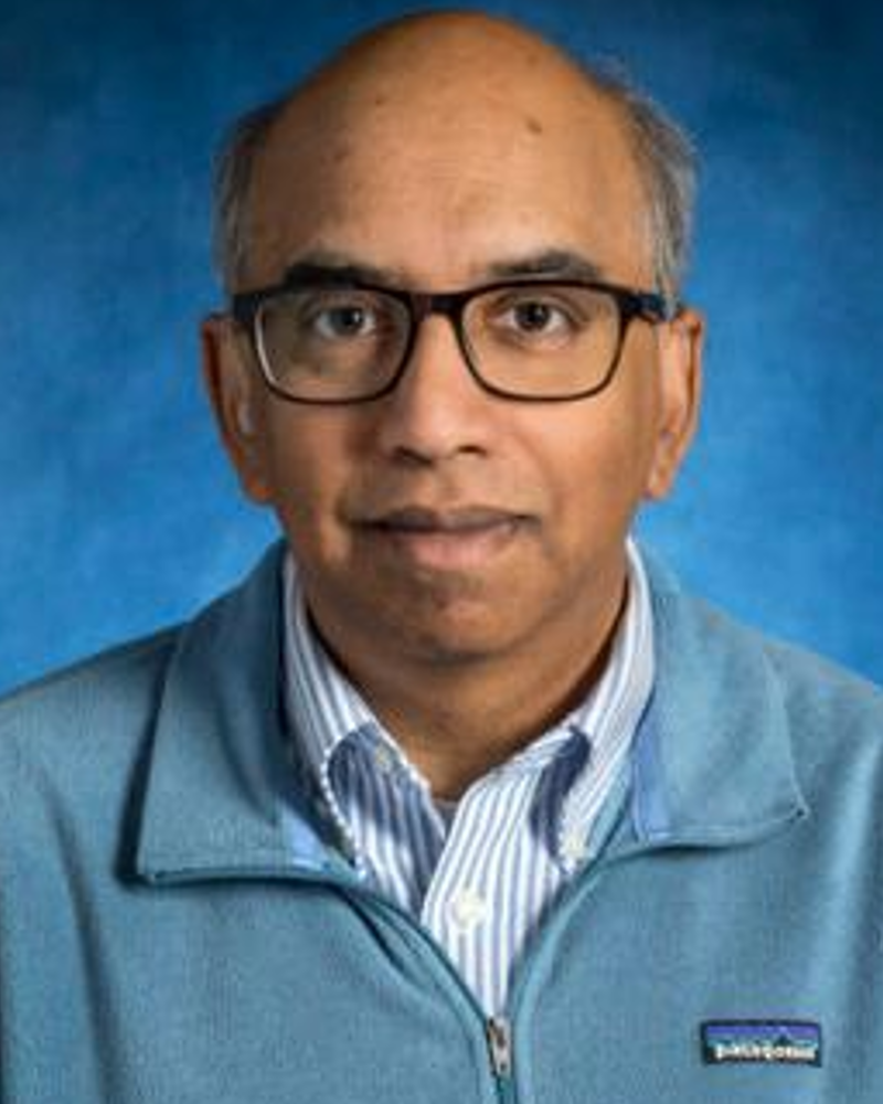 Head of Asian man with glasses, hearing aid and cochlear implant. Wearing striped shirt with light blue sweater. Hazy blue background.