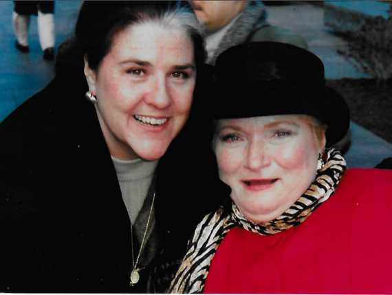 Susan Daniels on the right wearing a black hat, red winter coat and tiger-striped scarf with Marie Strahan on the left leaning in wearing a black winter coat, both smiling at the bill signing for the Ticket to Work and Work Incentives Improvement Act, December 17, 1999